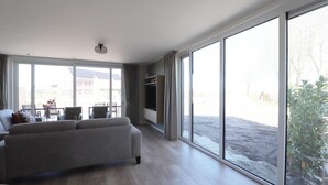 A spacious living room with a large sofa, a dining table, and a TV.