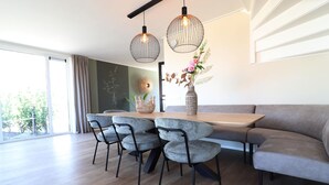 A modern dining area with a wooden table, four grey chairs, a grey sofa, and two pendant lights.