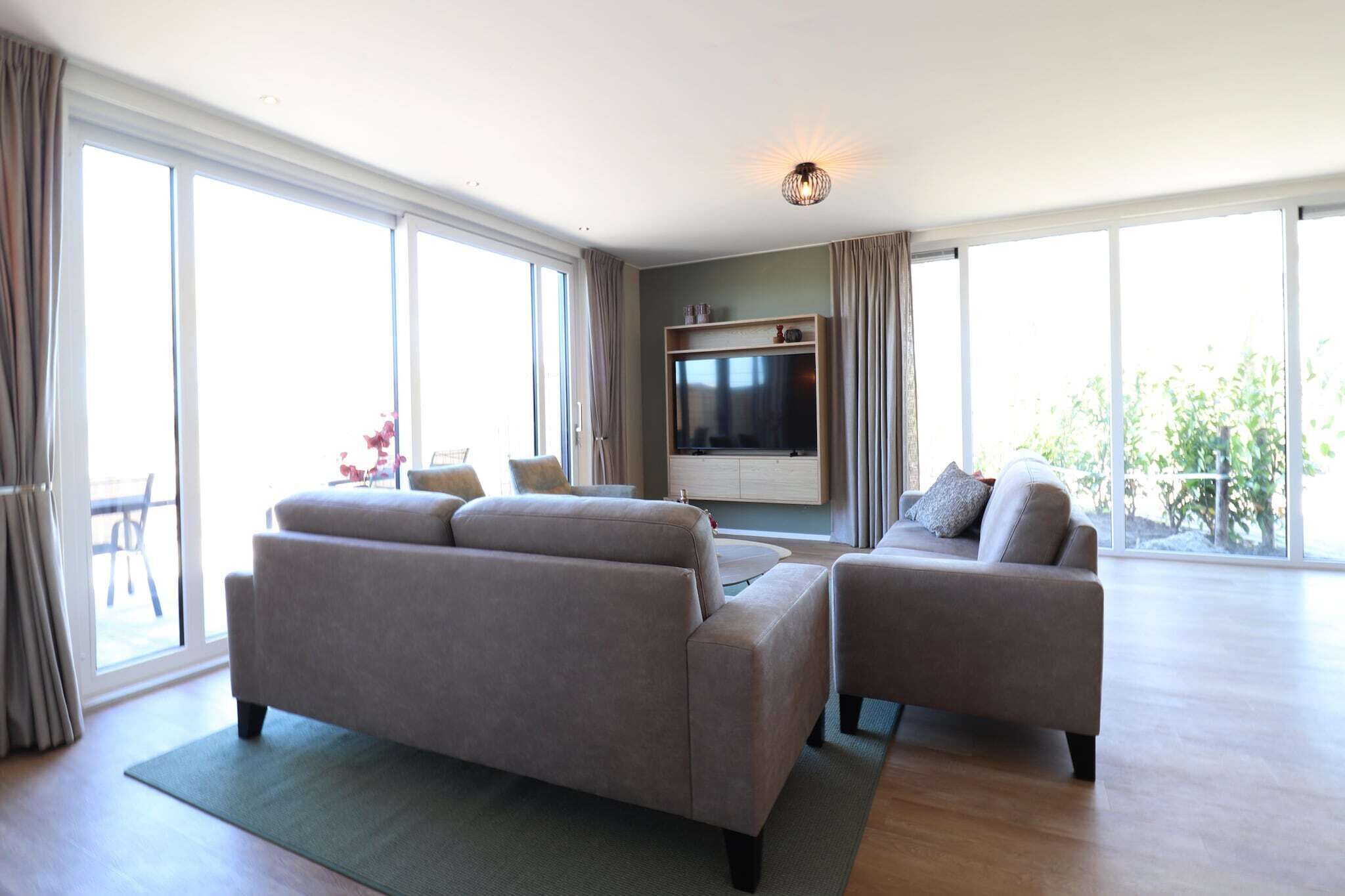 Un salon moderne avec deux canapés, un téléviseur à écran plat et une porte-fenêtre coulissante donnant sur un espace extérieur.