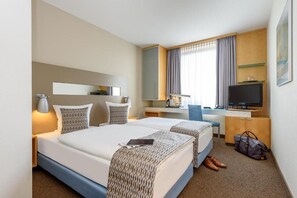 Una habitación de hotel con dos camas, un escritorio, un televisor y un armario.