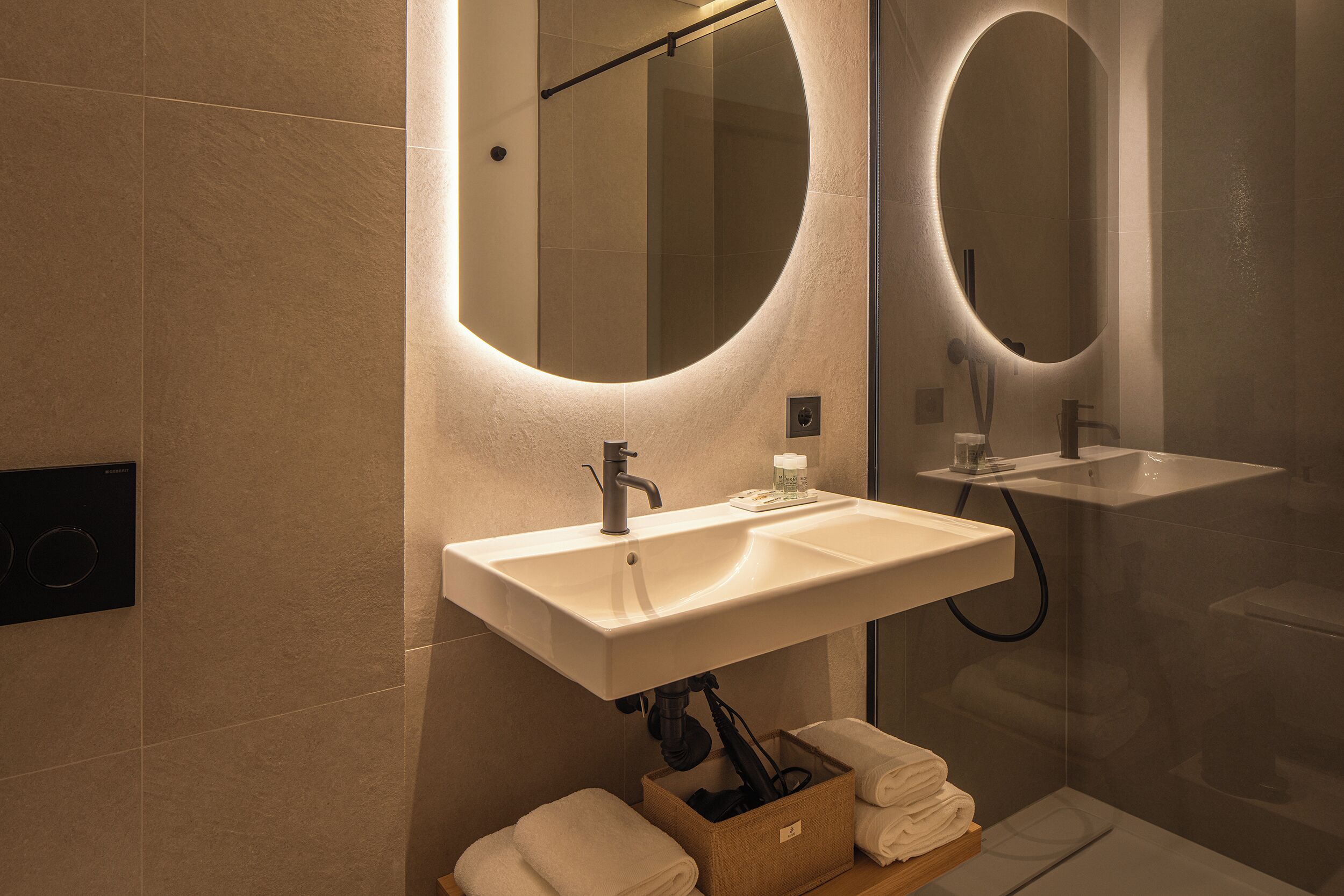 A modern bathroom with a large oval mirror, a sink, and a shower.