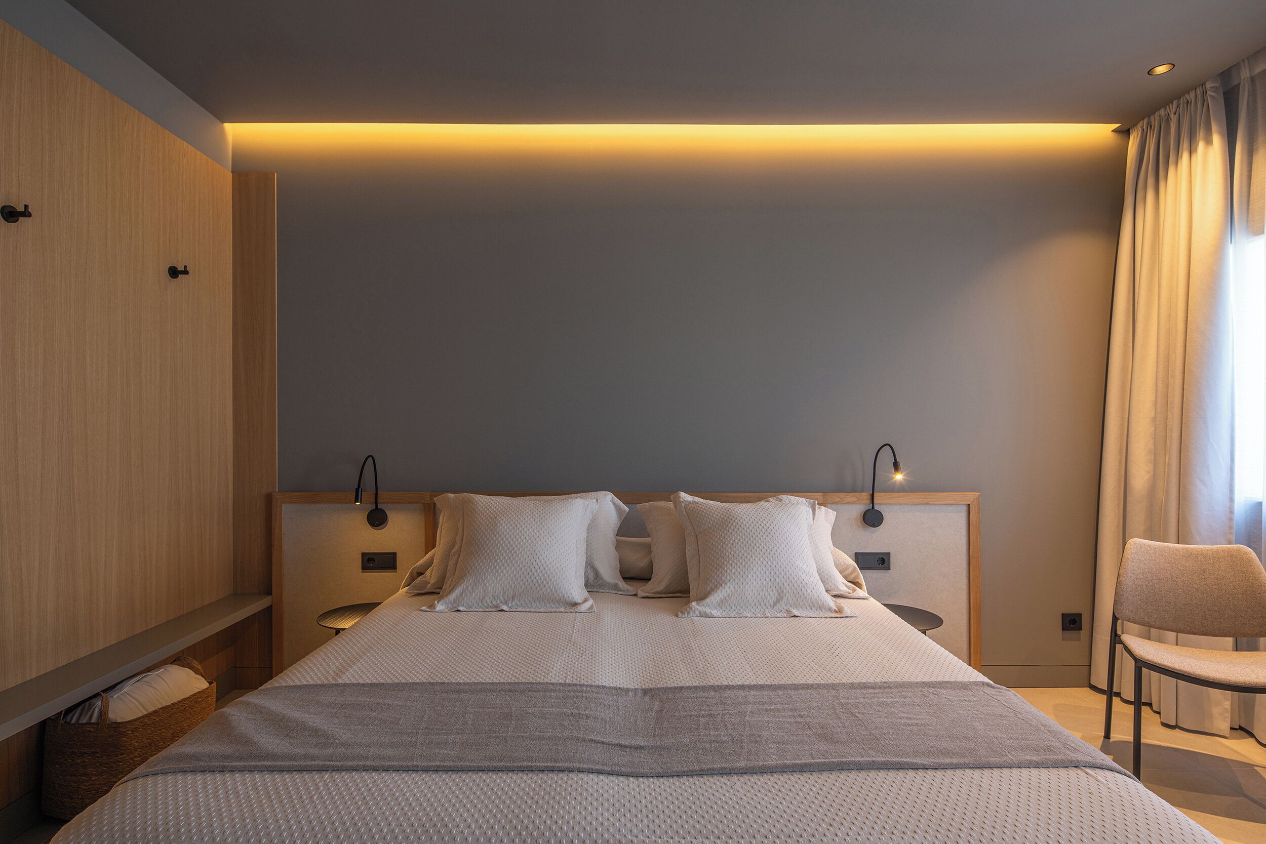 A modern hotel room with a large bed, bedside tables, a chair, and a built-in wardrobe.