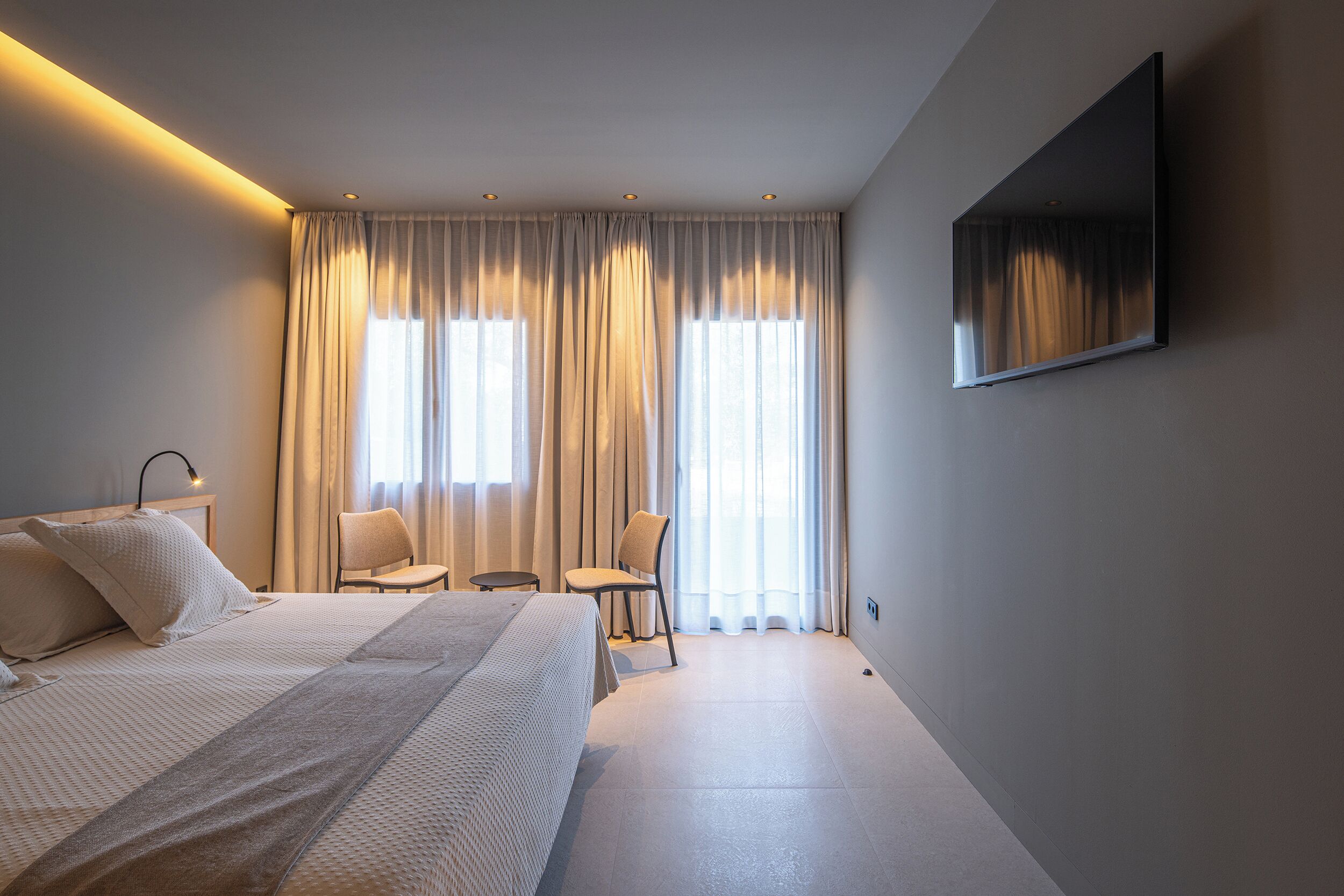 Une chambre d’hôtel moderne équipée d’un grand lit, d’un téléviseur à écran plat, d’une chaise et d’une petite table.