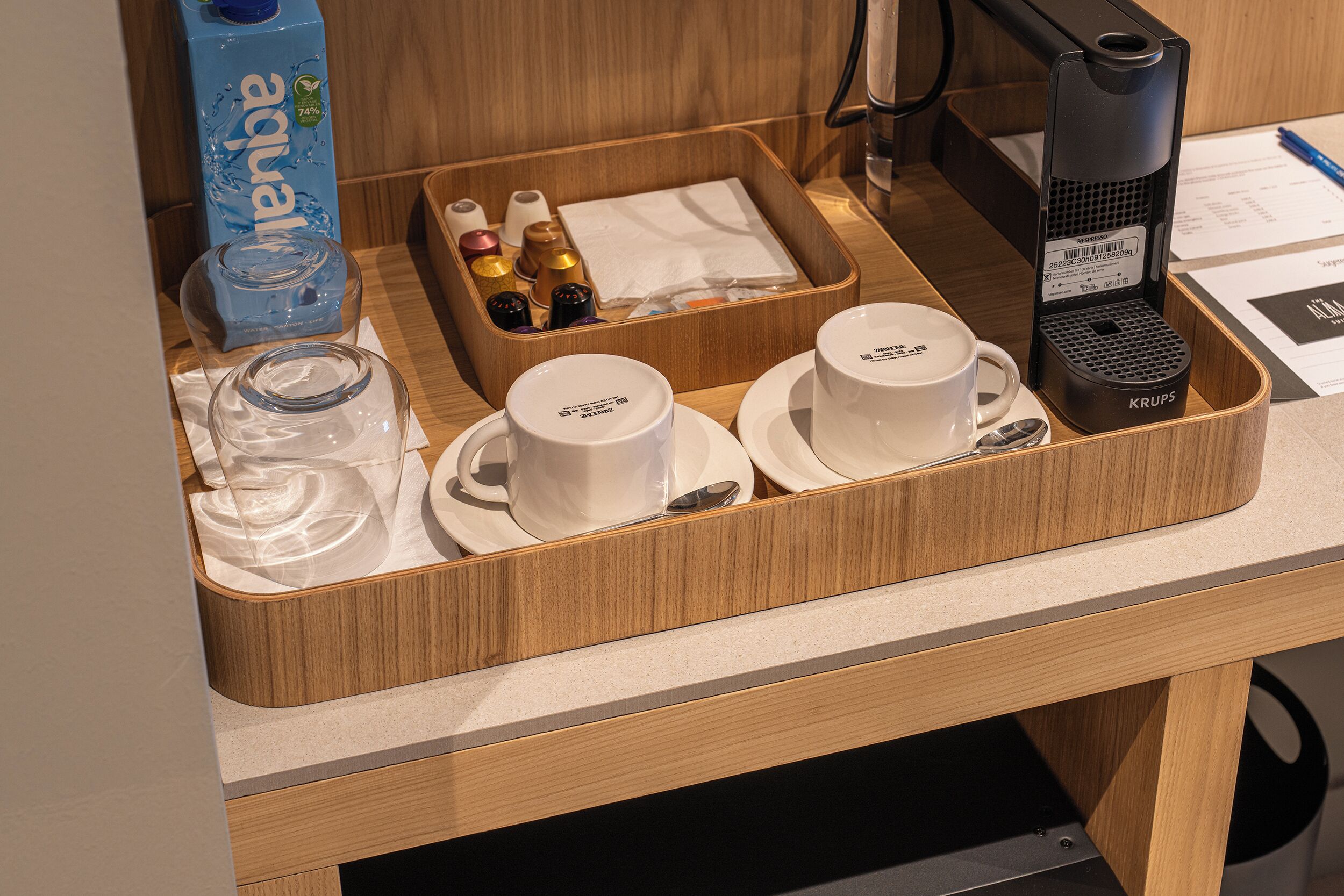 Ein Frühstücksbuffet im Hotelzimmer mit einer Krups-Kaffeemaschine, einem Wasserspender und einem Tablett mit Tassen und Beilagen.