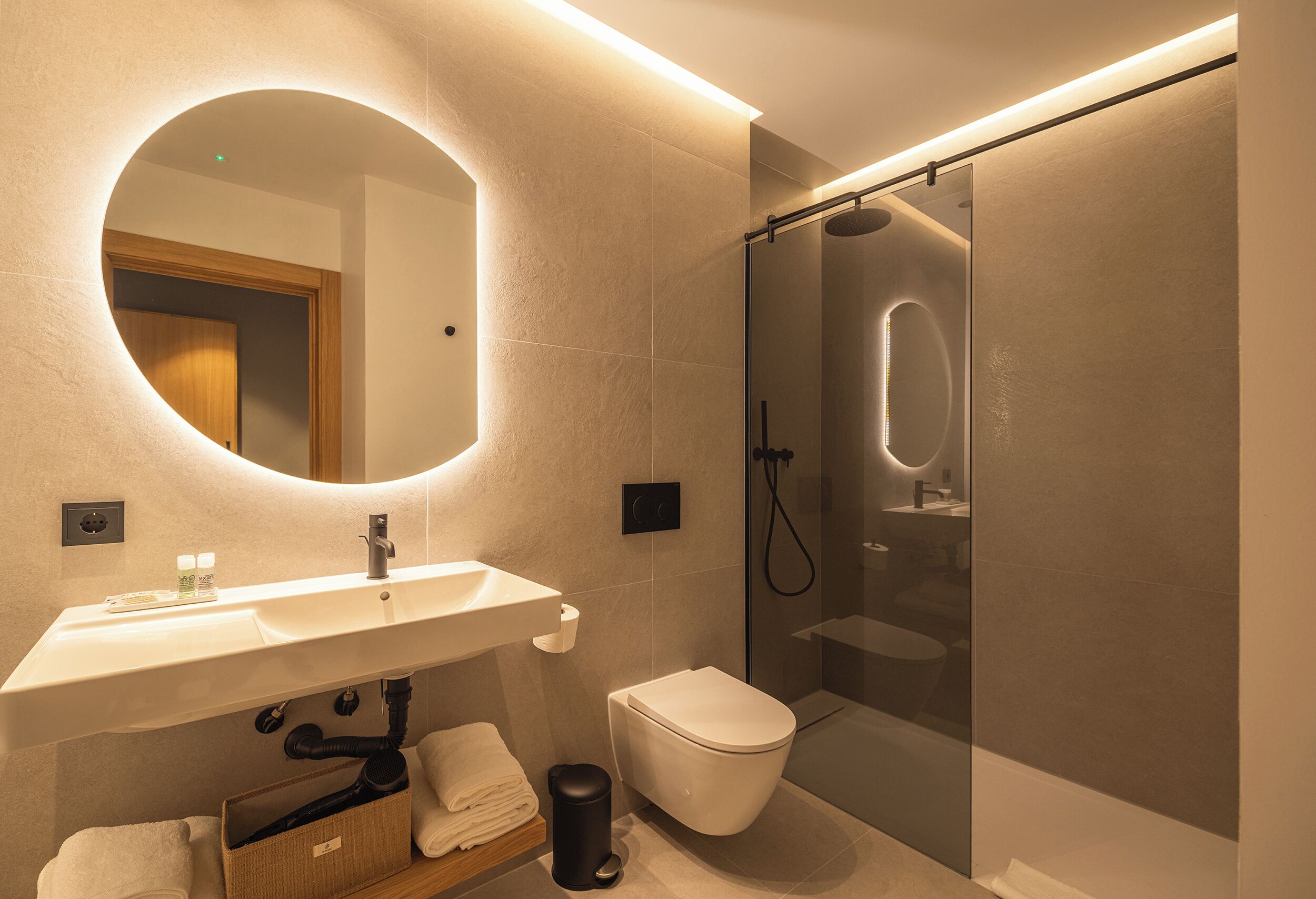 A modern bathroom with a round mirror, a sink, a toilet, and a glass-enclosed shower.