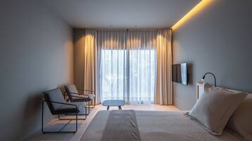 A modern hotel room with a bed, a seating area with chairs, a small table, and a TV mounted on the wall.