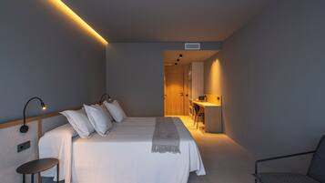 Un dormitorio con cama, mesita de noche, silla y un espacio de escritorio con otra silla.