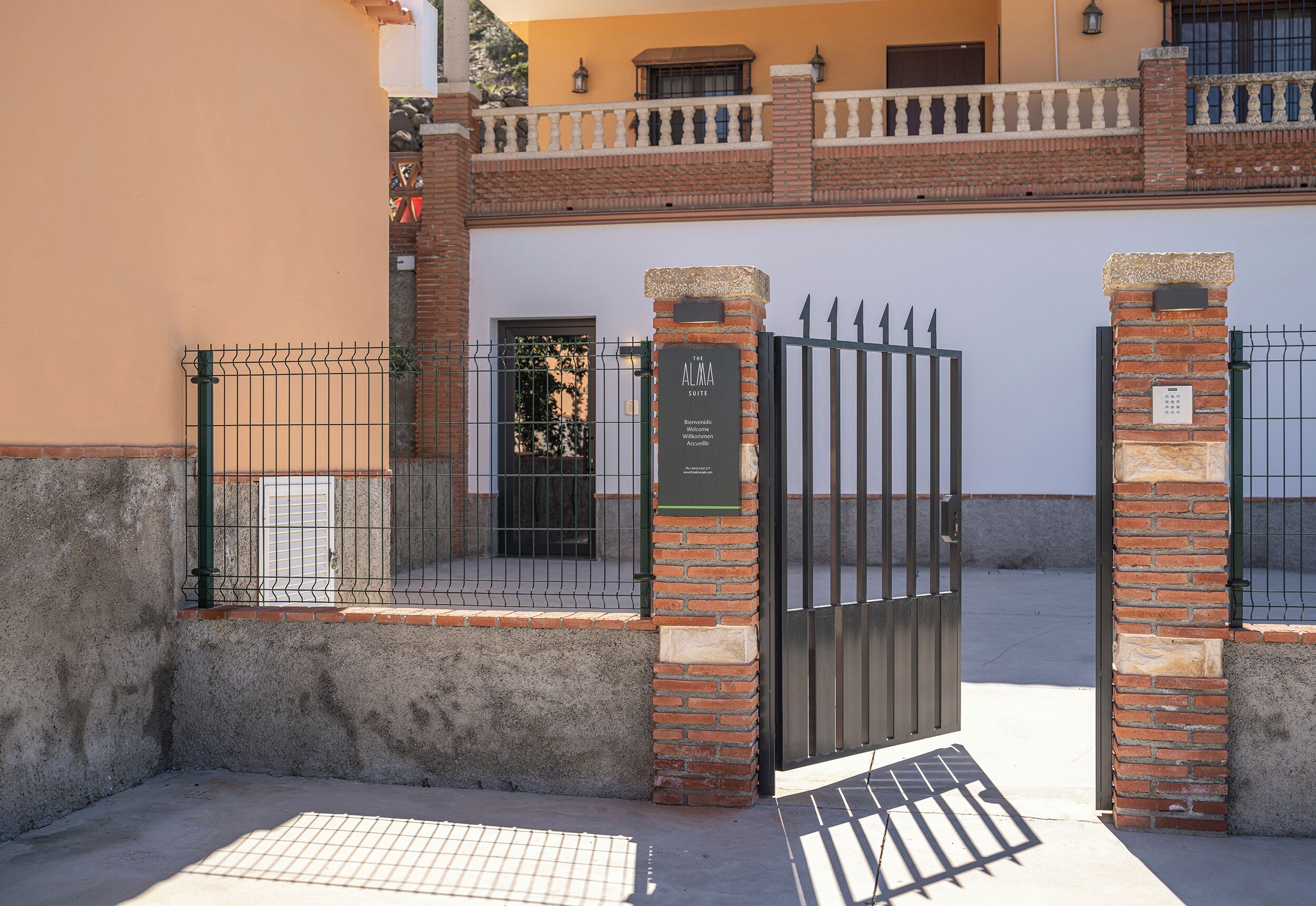 A gated entrance with a sign, a brick wall, and a balcony.