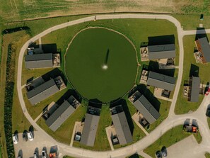 Eine Vogelperspektive zeigt einen kreisförmigen Gebäudekomplex mit einem zentralen Teich, umgeben von mehreren Gebäuden mit flachen Dächern, die in einer strahlenförmigen Anordnung angeordnet sind.