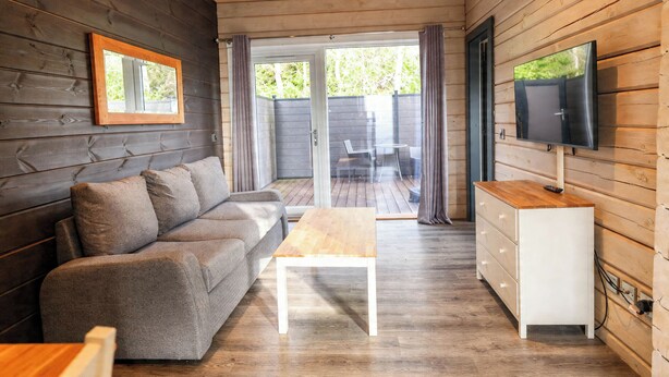 Een gezellig interieur van een chalet met een bank, een houten bijzettafeltje, een aan de muur bevestigde televisie en een schuifdeur naar buiten.