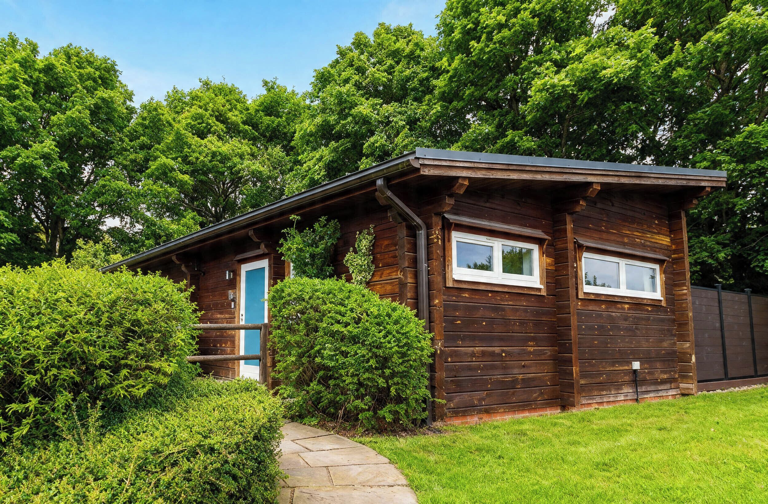En stuga byggd av trä med en blå dörr, omgiven av frodig grönska och en stig av sten.