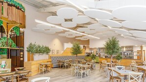 Een restaurantinterieur met ronde tafels, zachte zitplaatsen en een keuken op de achtergrond.