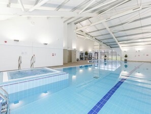 Ein Hallenbad mit klarem Wasser, geflieste Wände und hoher Decke.