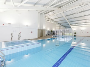An indoor swimming pool with clear water, tiled walls, and a high ceiling. - Pine Lodge Spa (Thirsk)