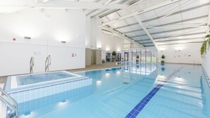 En inomhuspool med tydligt markerade banor, ett kaklat golv och ett högt tak med synliga bärande balkar.