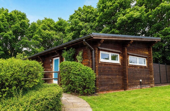 A wooden cabin with a blue door, surrounded by lush greenery and a stone pathway. - Pine Lodge Spa (Thirsk)