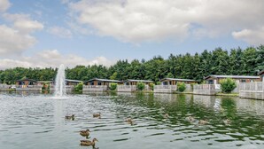Ein See mit Enten, einem Brunnen und Holzblockhäusern.