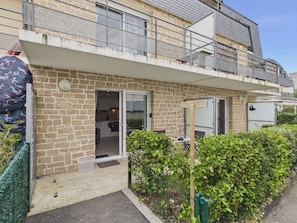 A two-story building with a brick facade, a balcony with a metal railing, and a small garden area with a hedge.