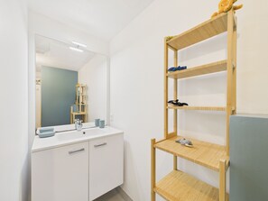 A bathroom with a white vanity, a mirror, and a wooden shelf with plush toys.