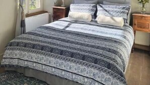 Een slaapkamer met een groot bed, een raam met gordijnen, een houten hoofdbord en een nachtkastje met een lamp.