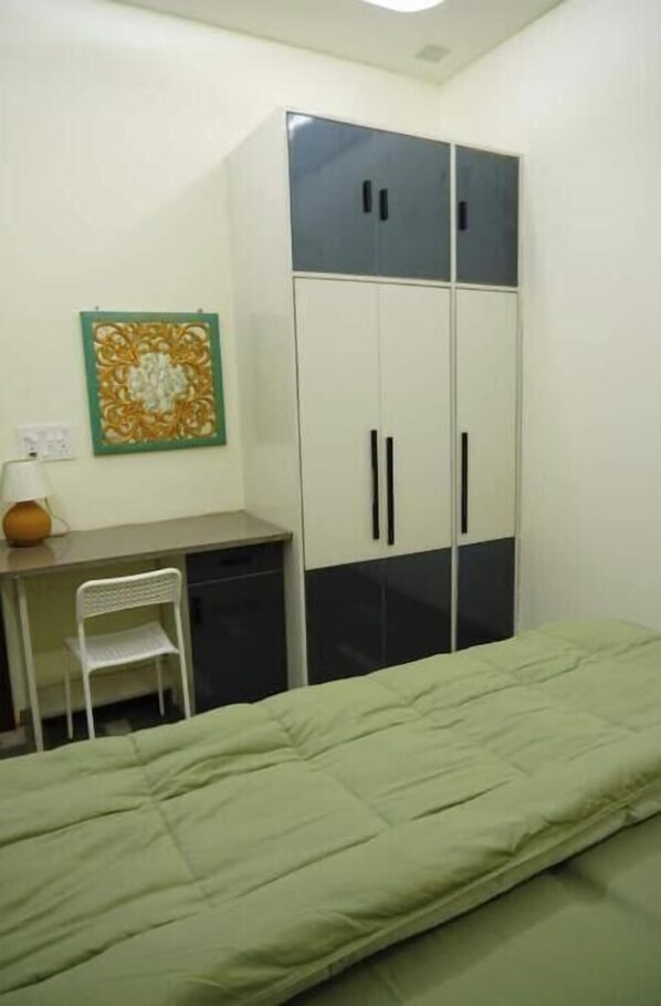 A bedroom with a bed, a desk with a chair, a wardrobe, and a wall-mounted lamp.