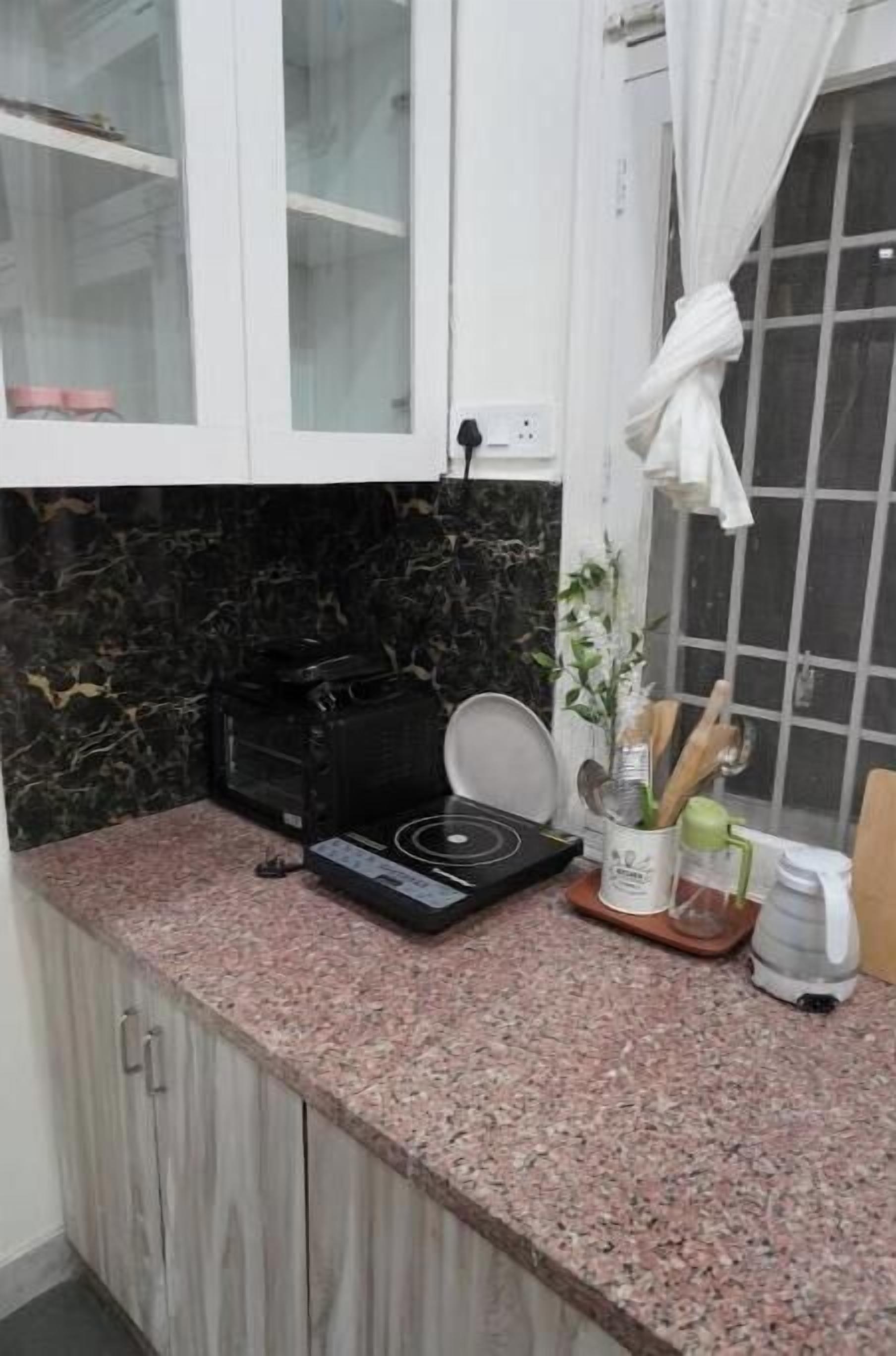 A kitchen with a granite countertop, a black electric stove, and a white cabinet with glass doors.