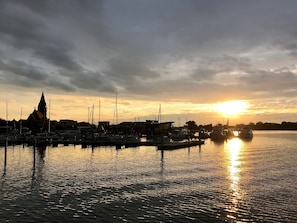 A marina with boats docked, a church spire, and a sunset over the water. - Bungalow in a Green Setting—with a Fireplace and 2 Terraces (Pruchten)
