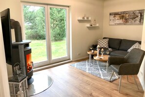 A living room with a fireplace, a sofa, a coffee table, and a view of the outdoors. - Time out near the Baltic Sea - tastefully furnished, with terrace & wood-burning stove (Pruchten)