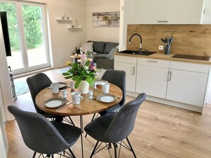 A dining area with a round table set for four, surrounded by chairs, a vase of flowers, and a kitchen with white cabinets and a wooden countertop. - Time out near the Baltic Sea - tastefully furnished, with terrace & wood-burning stove (Pruchten)