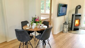 A dining area with a round table, four chairs, a vase of flowers, and a fireplace. - A Cozy Getaway in the Countryside — 2 Bedrooms & a Fireplace (Pruchten)
