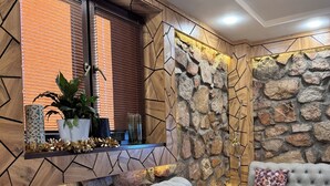 Una sala moderna con un sofá gris capitonado, una pared de acento de piedra y una ventana con persianas.