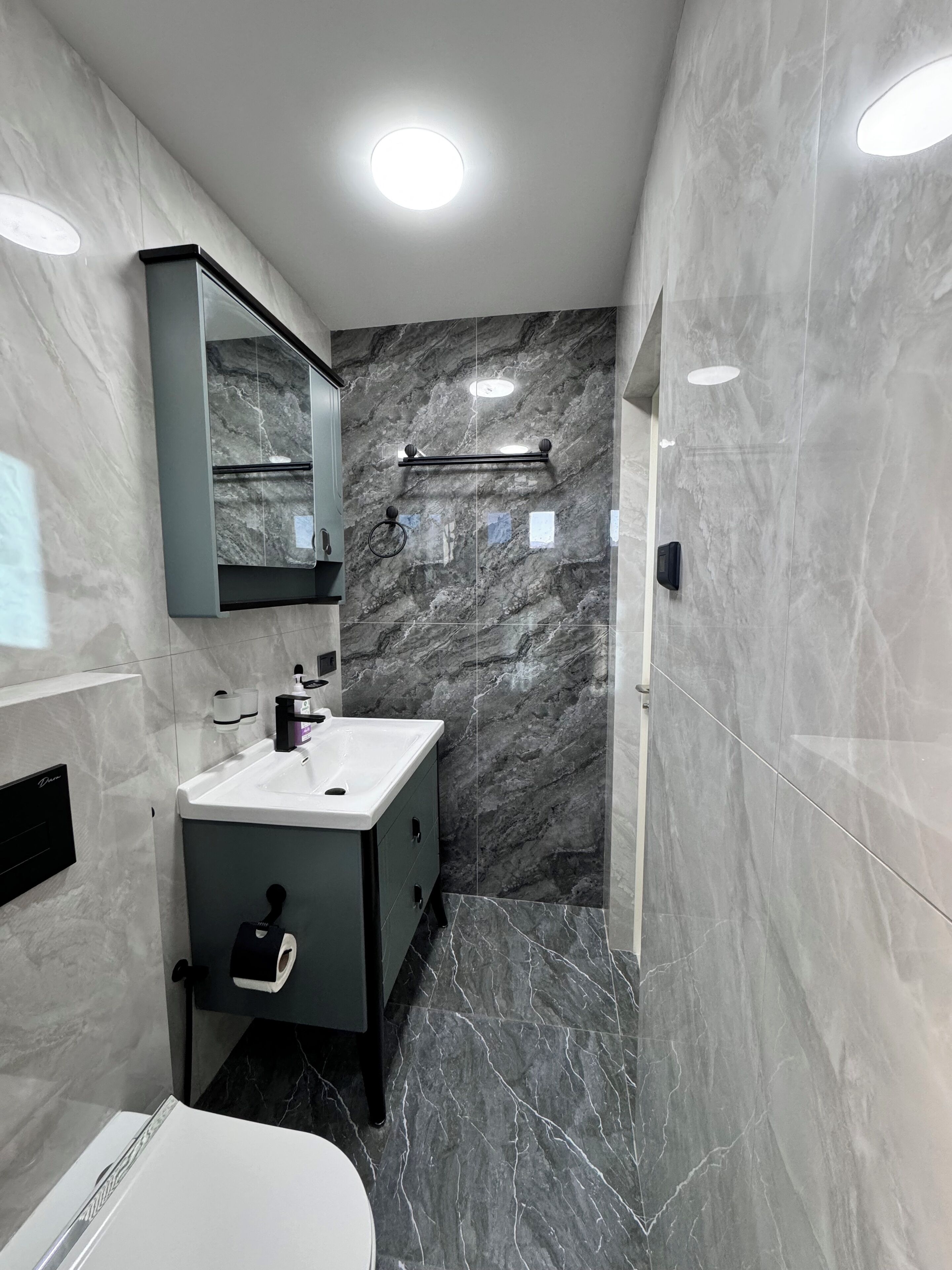 Un baño moderno con tocador de mármol, espejo, perchero y zona de ducha.