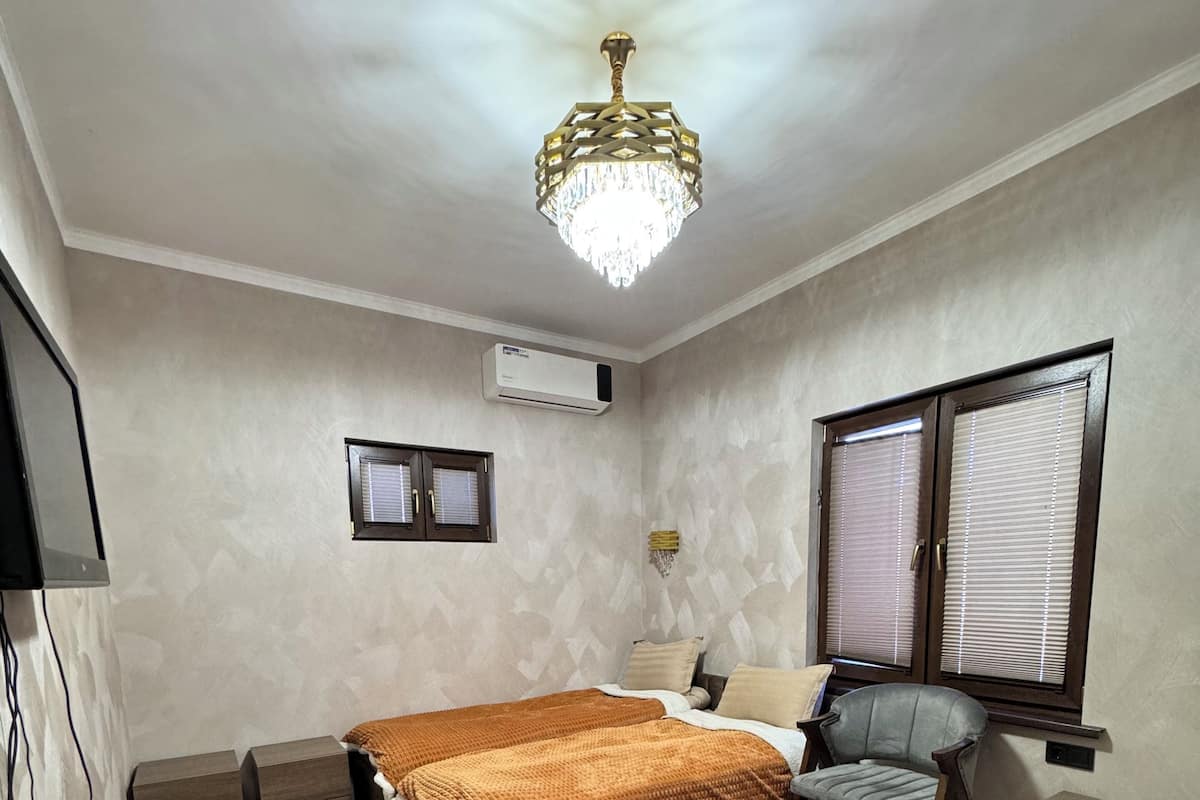A bedroom with two beds, a chair, a bedside table, an air conditioning unit, and a ceiling light fixture.