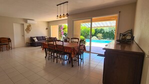 Ein geräumiger Wohnbereich mit Esstisch, Stühlen, einer Couch und Blick auf einen Swimmingpool.