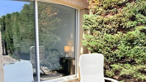 Een terras met rieten meubels, waaronder twee stoelen en een bijzettafeltje, dichtbij een schuifpui.