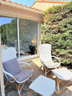Un espace patio aménagé avec des meubles en osier, comprenant deux chaises et une petite table, situé près d’une porte-fenêtre coulissante.