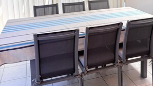 Een overdekt terras met een tafel, stoelen, houten balken en een raam met zonwering.