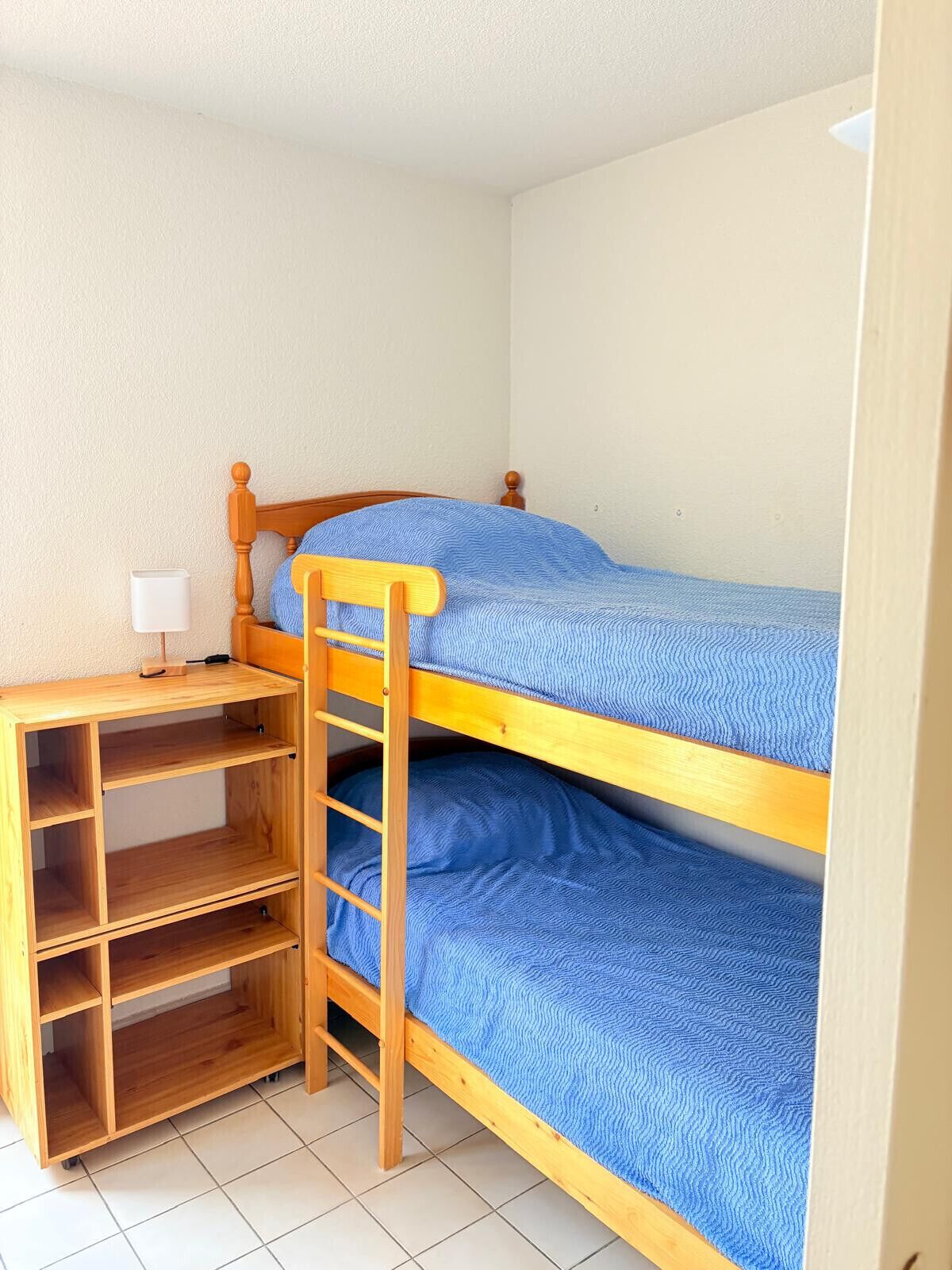 A bunk bed with a wooden ladder, a desk with a lamp, and a shelf unit.
