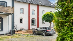 Un bâtiment à deux étages avec une bande verticale rouge, une voiture garée devant et un petit arbre.