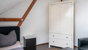 Une chambre avec un plafond en pente, un lit avec des oreillers, une armoire blanche et une petite table de chevet.
