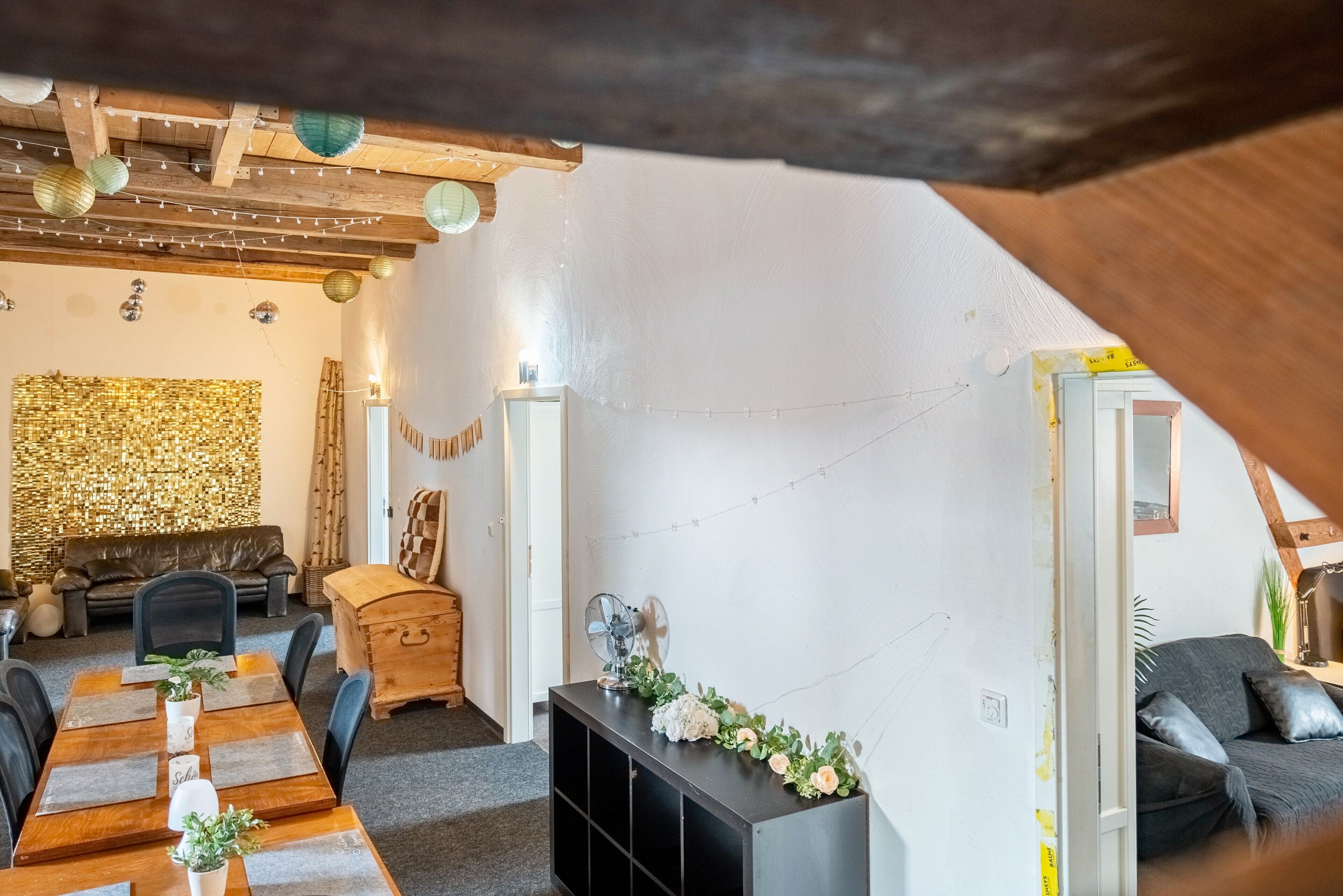 Ein gemütliches Wohnzimmer mit Holzbalkendecke, einer Couch, einem Esstisch mit Stühlen und einer schwarzen Unterhaltungseinheit.