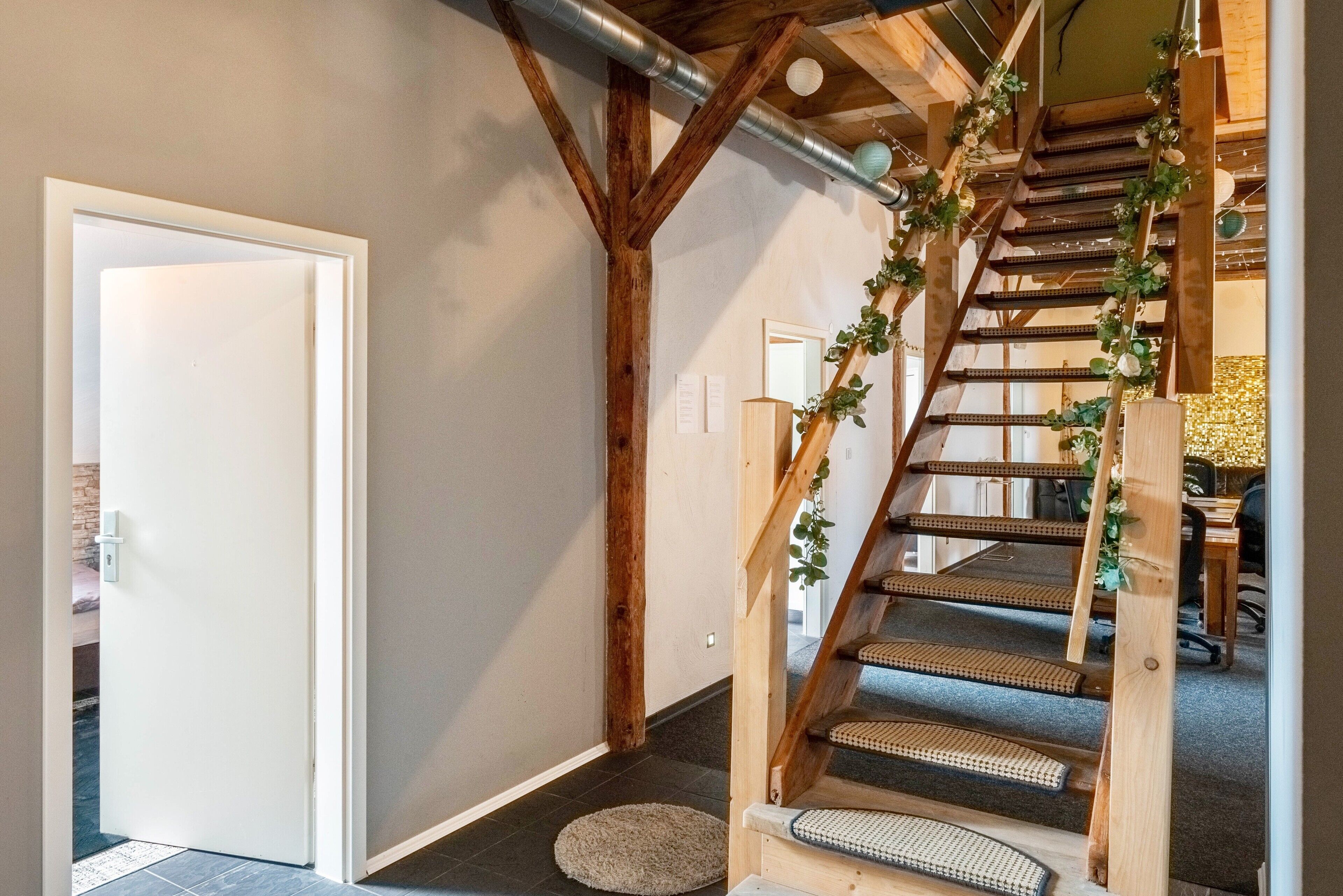 Eine Holztreppe mit Handlauf, eine weiße Tür und ein kleiner Teppich auf dem Boden.