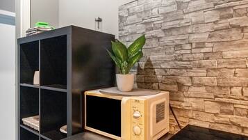A microwave oven with a plant on top, a black shelving unit, and a stone-textured wall.