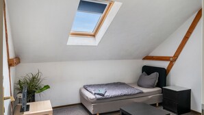 Une petite pièce avec un plafond en pente, comprenant un lit, un bureau, une chaise et une fenêtre.