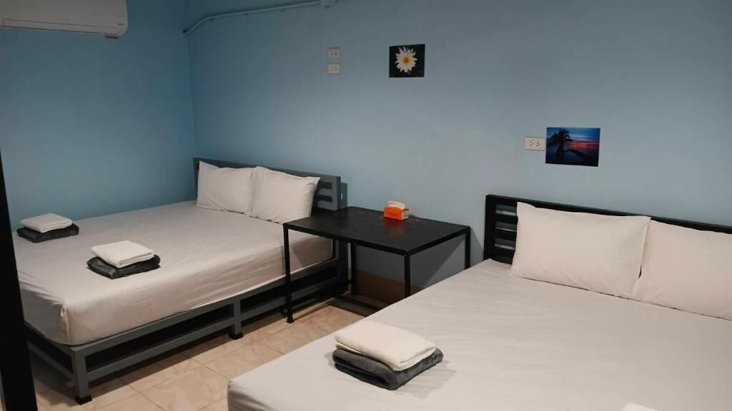 A room with two beds, a small table, and a wall-mounted air conditioner.