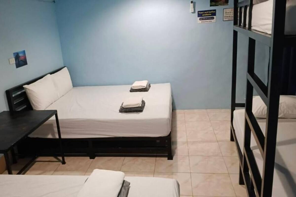 A single-bed room with a desk, a bed with pillows, a bunk bed, and a sign indicating breakfast and coffee availability.