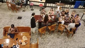 A group of people seated around a wooden table in a room with a stone floor, chairs, and a sofa. - Dee-maak Hostel (Ko Pha-ngan)