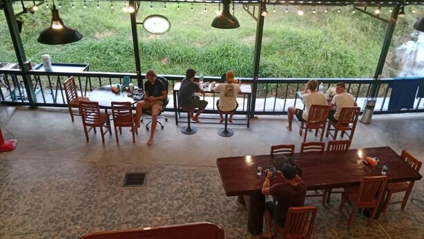 An outdoor dining area with tables and chairs, surrounded by a railing with a view of greenery. - Dee-maak Hostel (Ko Pha-ngan)