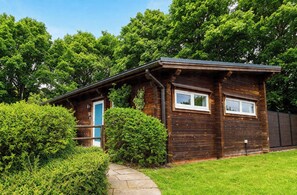 A wooden cabin with a blue door, surrounded by lush greenery and a stone pathway. - Pine Lodge Spa Pet (Thirsk)
