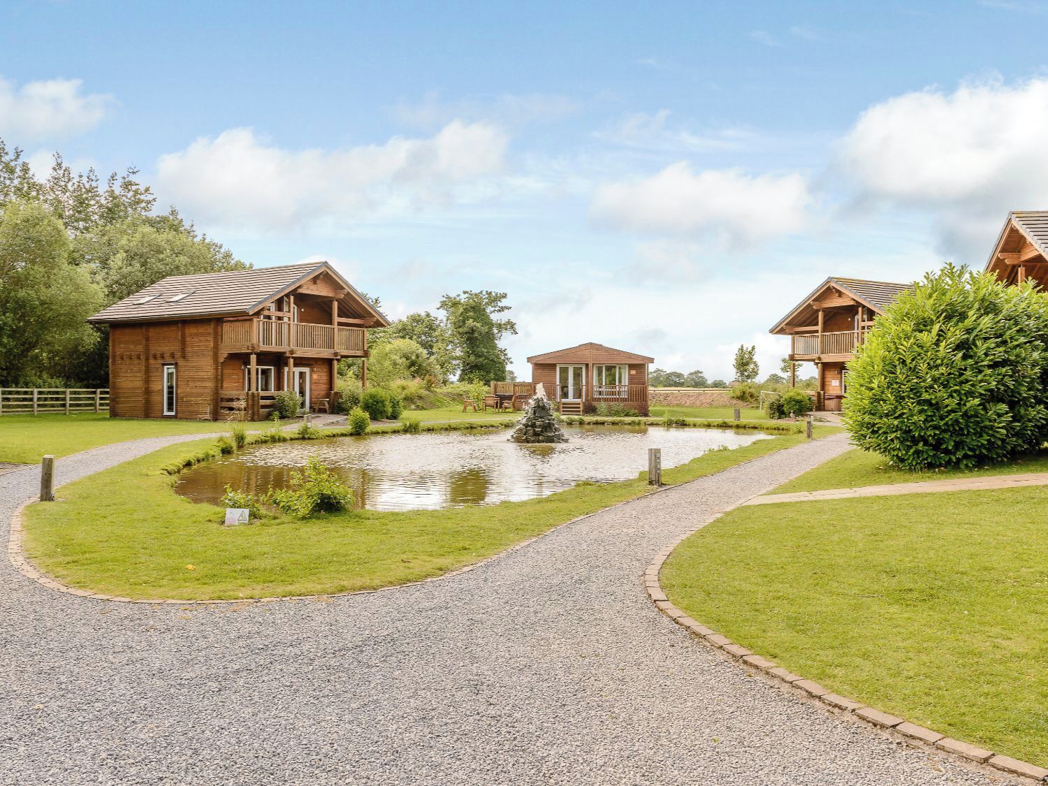 A wooden lodge with a gravel path, a pond, and a small bridge.
